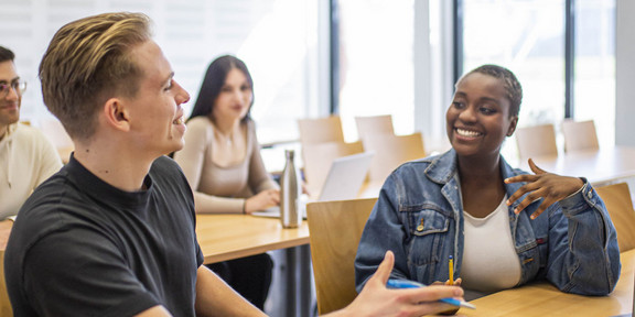 Studierende sitzen im Seminarraum und reden miteinander.